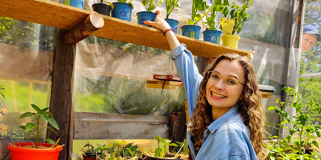 Pflanzensprechstunden-Beraterin Franzi des nachhaltigen Start-ups primoza steht umringt von Pflanzen in einem Gewächshaus und lächelt in die Kamera