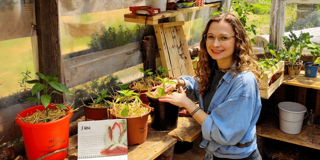 Pflanzensprechstunden-Beraterin Franzi des nachhaltigen Start-ups primoza steht umringt von Pflanzen in einem Gewächshaus und lächelt in die Kamera