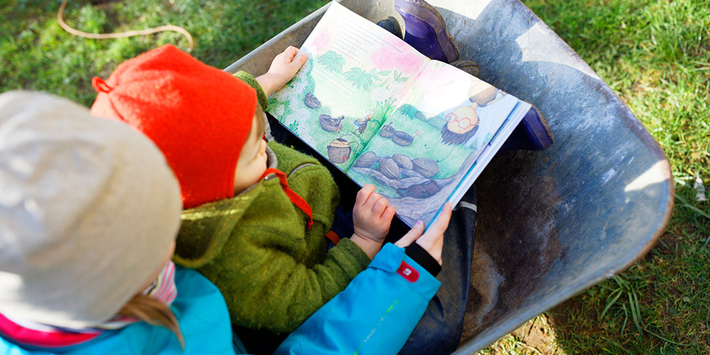 Kinder sitzen in einer Schubkarre und lesen das nachhaltige und interaktive Kinderbuch Emi Brillenbiene von primoza