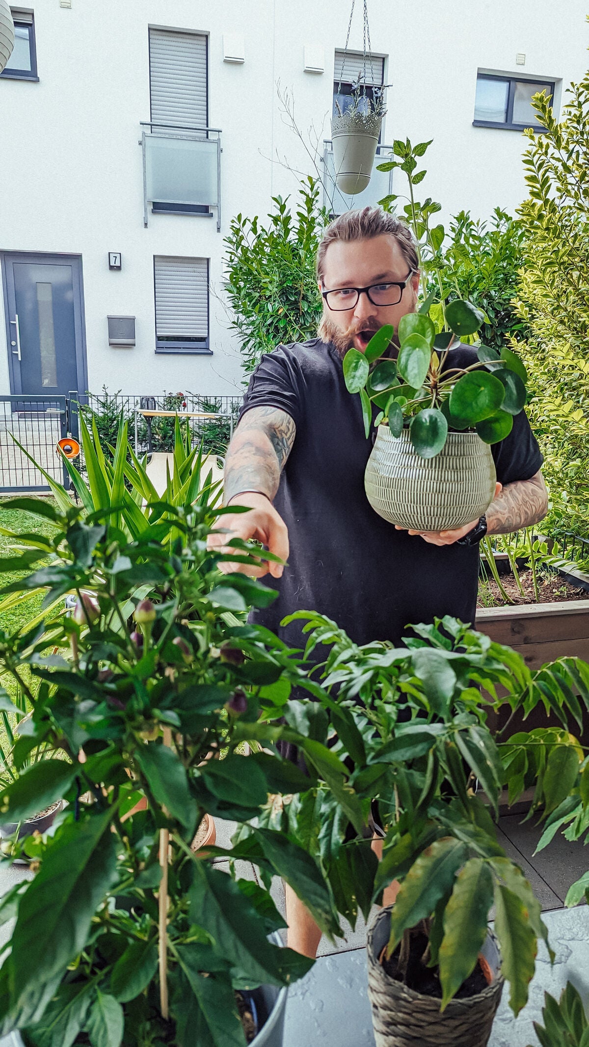 Steff zeigt überrascht auf eine Chili und hält eine Pflanze in der anderen Hand